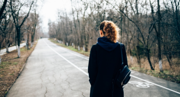 Een vrouw wandelt over de weg. Alleen haar rug en tas zijn zichtbaar.